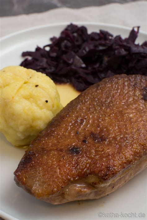 A White Plate Topped With Meat Potatoes And Red Cabbage Next To An