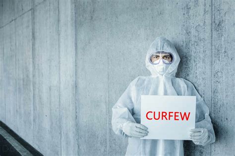 Portrait Of Man Wearing Protective Clothing Holding A Curfew Sign