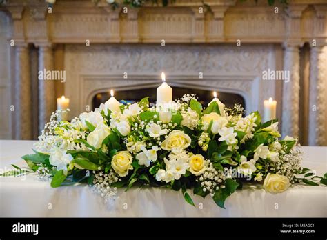 Cream floral arrangement with lit candles on wedding reception table ...