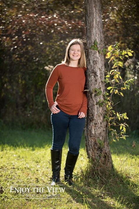 A Woman Standing Next To A Tree With Her Hands On Her Hips And Smiling