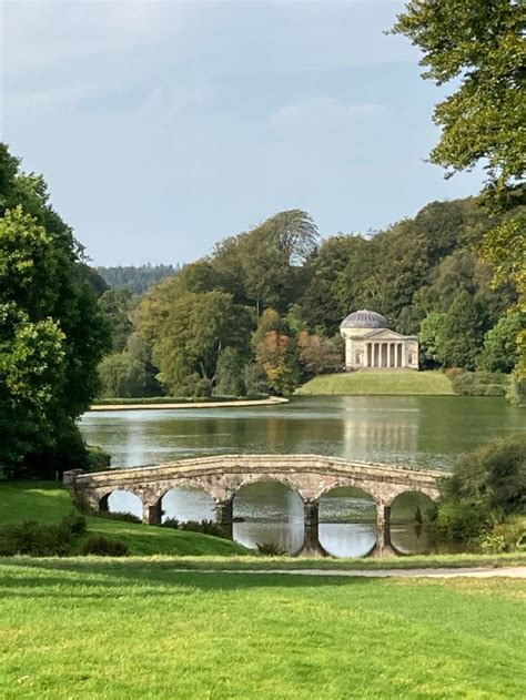 a stone bridge crossing over a lake in the middle of a lush green park area