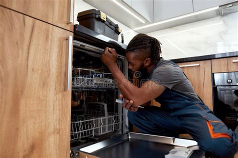 Young African Repairman Repairing Dishwasher In Kitchen Using