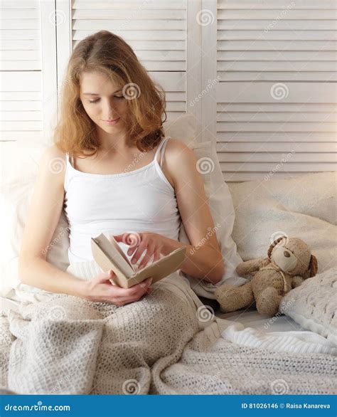 Jeune Femme Se Situant Dans Le Lit Tout En Lisant Un Livre Photo Stock