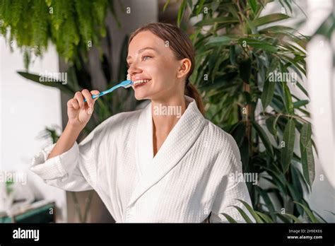 Pretty Young Woman Brushing Her Teeth In Front Of A Mirror In The