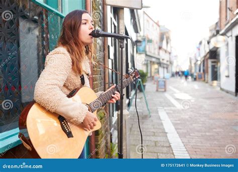 Female Musician Busking Playing Acoustic Guitar And Singing Outdoors In