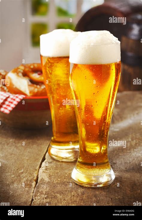 Two Tall Glasses Of Golden Ale Or Beer With A Good Head Of White Froth On An Old Wooden Kitchen