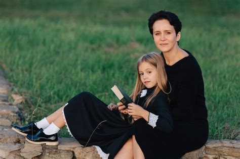 Mãe e filha estão sentadas em um banco de pedra e lendo um livro