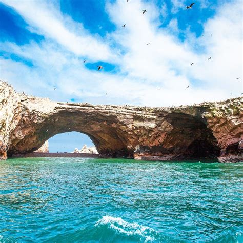 Birds Fly Over The Water Near An Arch In The Rock Formation That