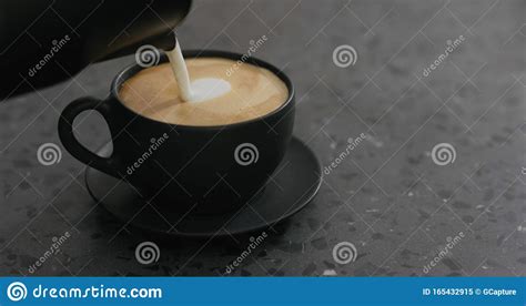 Pouring Steamed Milk Into Cappuccino In Black Cup On Terrazzo