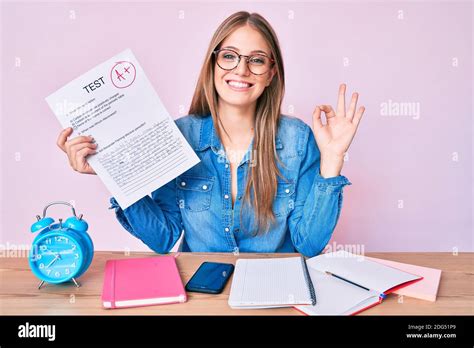 Junge blonde Mädchen zeigt bestanden Prüfung sitzen auf dem Tisch tun