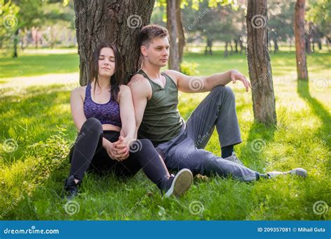 Athletic Guy And Girl Sitting On The Lawn Leaning Against A Tree Stock