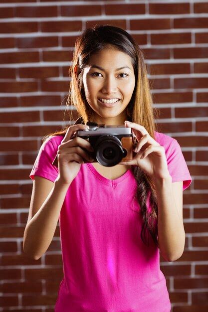 Mujer asiática sonriente que toma la imagen con la cámara en la pared