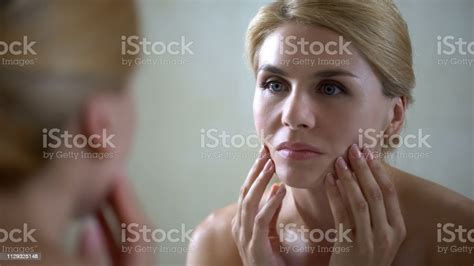 Upset Woman Looking In Mirror And Touching Face Sad About Skin Aging