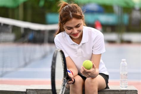 Bastante Joven Deportista Sosteniendo Raqueta De Pelota Sentada En El