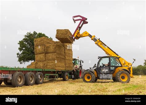 Man Using A Telehandler To Load Bales Of Straw Onto A Tractor Trailer