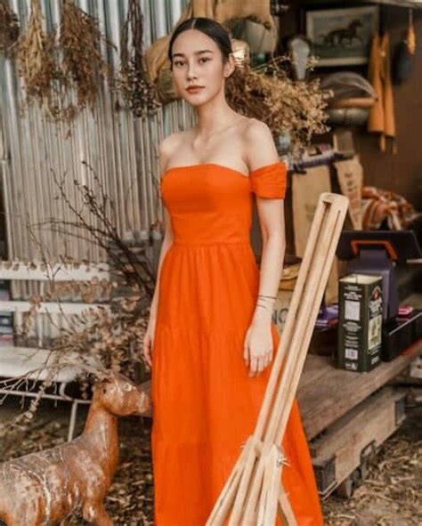 A Woman In An Orange Dress Standing Next To A Pile Of Bamboo Sticks And