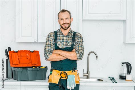 Smiling Handsome Plumber Standing With Crossed Arms And Looking At