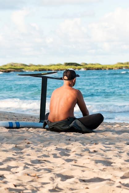 Homem sentado ao lado de sua prancha de surfe ao ar livre Foto Grátis