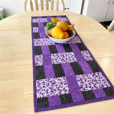 A Bowl Of Fruit Sitting On Top Of A Purple Table Runner Next To A Bowl Of Fruit