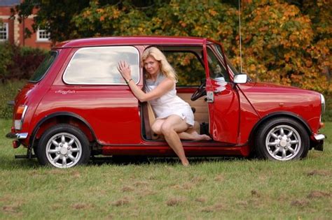 A Woman Is Sitting In The Open Door Of A Small Red Car With Her Hand Up