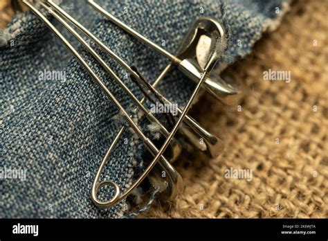 Safety Pins On A Strip Of Denim Against A Homespun Fabric With A Rough