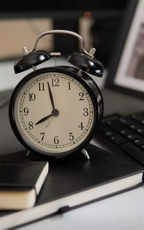 An Alarm Clock Sitting On Top Of A Desk Next To A Laptop