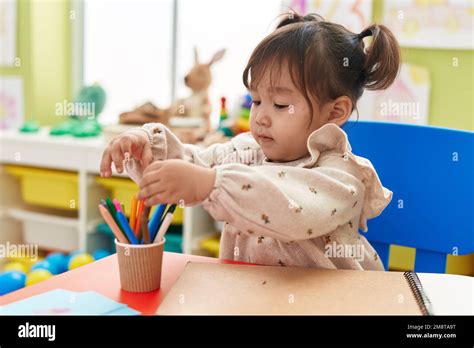 Adorable Chinese Girl Preschool Student Sitting On Table Holding Pencil