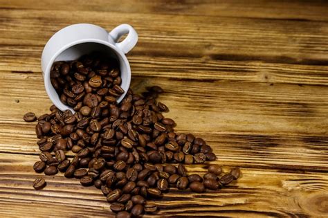 Premium Photo Roasted Coffee Beans Spill Out Of Cup On Wooden Table