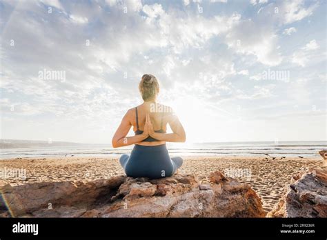 Woman Practicing Yoga With Hands Clasped Behind Back Sitting On Rock At