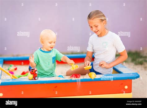 Cute Baby Boy Playing With His Sister With Toys In The Sandbox Outdoor