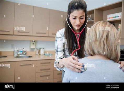 Female Doctor With Stethoscope Examining Patient In Exam Room Stock