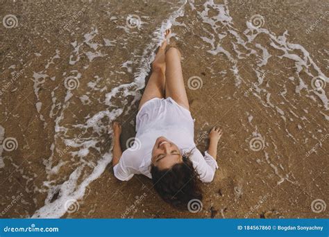 Happy Young Woman In White Shirt Lying On Beach In Splashing Waves Top