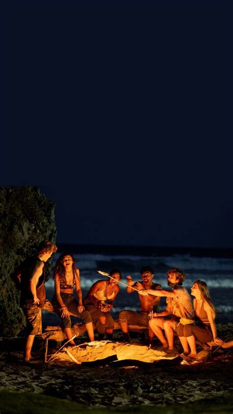 A Group Of People Sitting Around A Campfire On The Beach