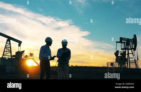 Two Engineers Working At Oil Field Surrounded By Oil Pumpjacks Stock