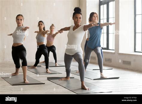 Group Of Young People Practicing Yoga Lesson Warrior 2 Pose Stock