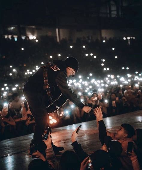 a man is performing on stage with his hands in the air while people are ...