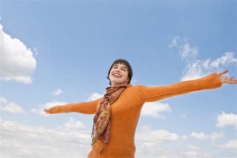 A smiling young woman standing with outstretched arms against the sky ...