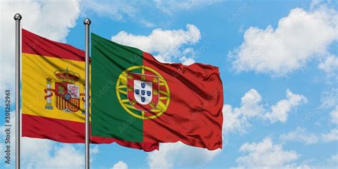 Spain and Portugal flag waving in the wind against white cloudy blue sky together. Diplomacy ...