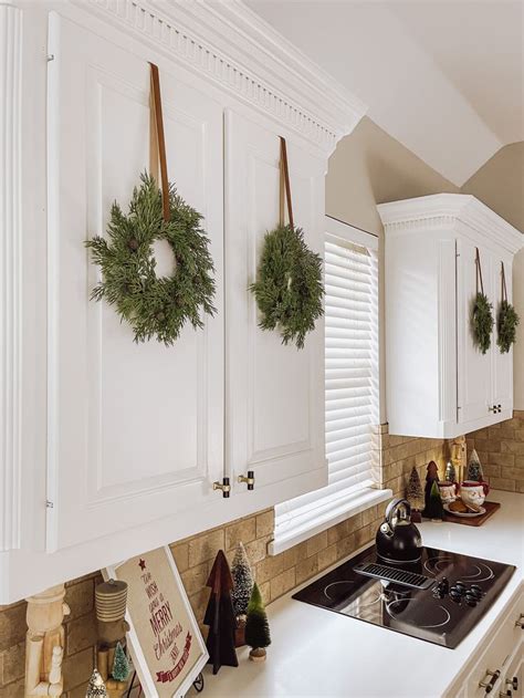 A Kitchen With White Cabinets And Wreaths Hanging On The Wall Above The