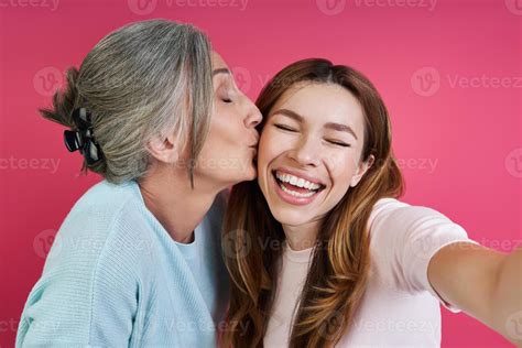 Senior Mother Kissing Her Cheerful Daughter While Making Selfie Against