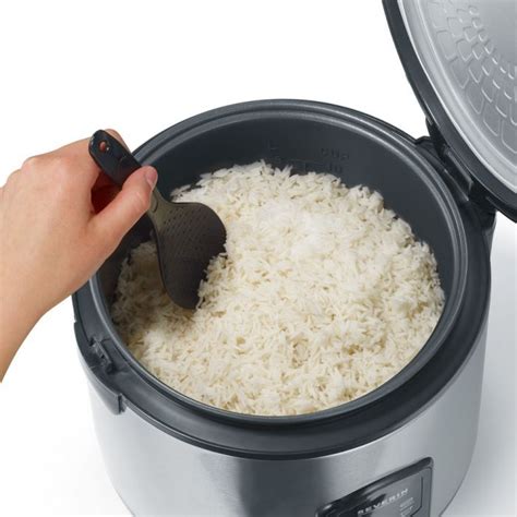 A Person Scooping Rice Into An Electric Pressure Cooker With Lid Open