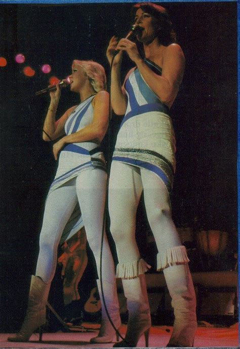 Two Women In White And Blue Outfits Singing On Stage With Microphones