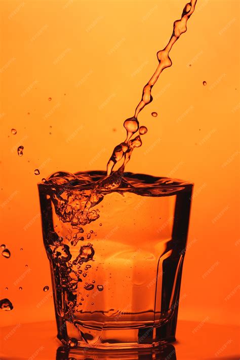 Premium Photo Pouring Water Into A Glass Splash Of Water In A Glass On Orange Background