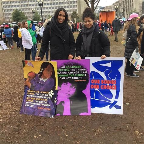 Two Women Holding Up Signs In Front Of A Group Of People On A Field