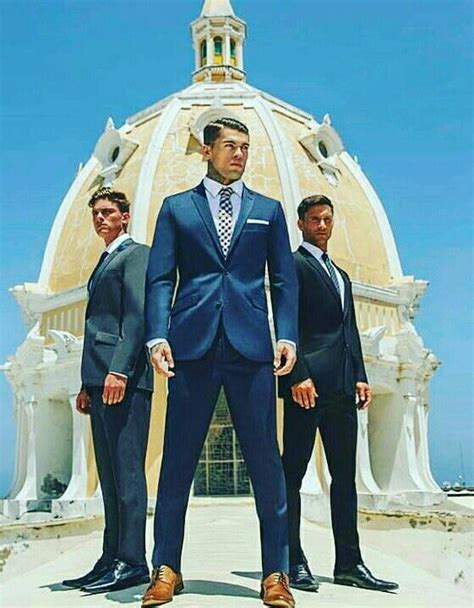 Three Men In Suits Standing Next To Each Other Near A Building With A