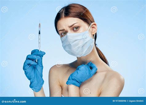 Young Beautiful Woman In Medical Mask And Rubber Gloves Holds Syringe On Blue Background