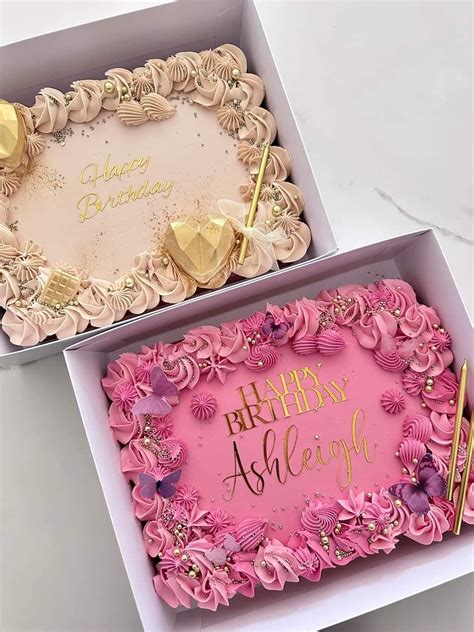 Two Pink Birthday Cakes In Boxes With Gold Writing On The Top And One