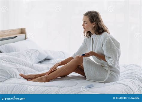 Woman Applying Lotion Cream On Her Legs On The Bed In Bedroom Stock