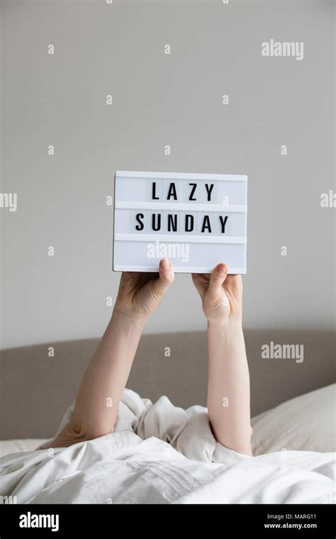 Female in bed under the sheets holding up a lazy sunday sign Stock ...