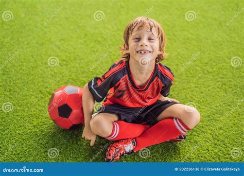 Little Cute Kid Boy In Red Football Uniform Playing Soccer Football On